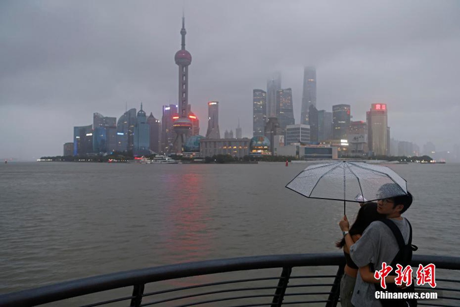I turisti ammirano gli edifici su entrambi i lati del fiume Huangpu durante il tifone sul Bund Riverside Trail a Shanghai. (Foto/Yin Liqin)